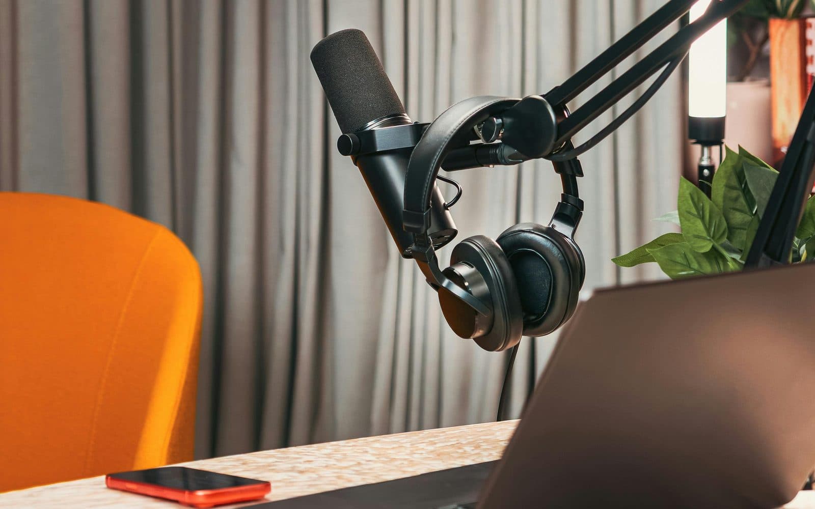 Podcast microphone and headphones on a boom arm beside a laptop in a home studio