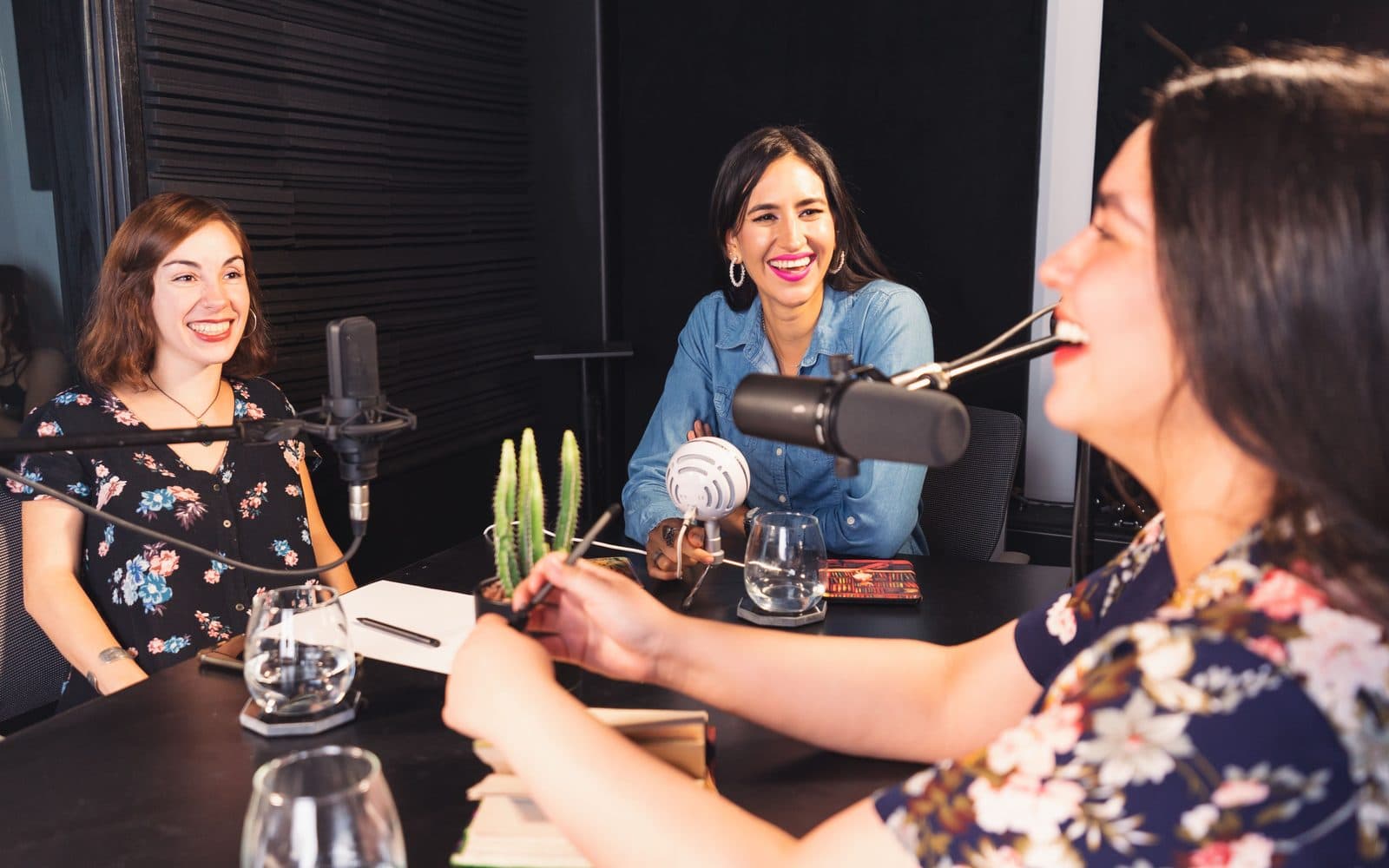 Three people laughing together during a podcast recording around studio microphones