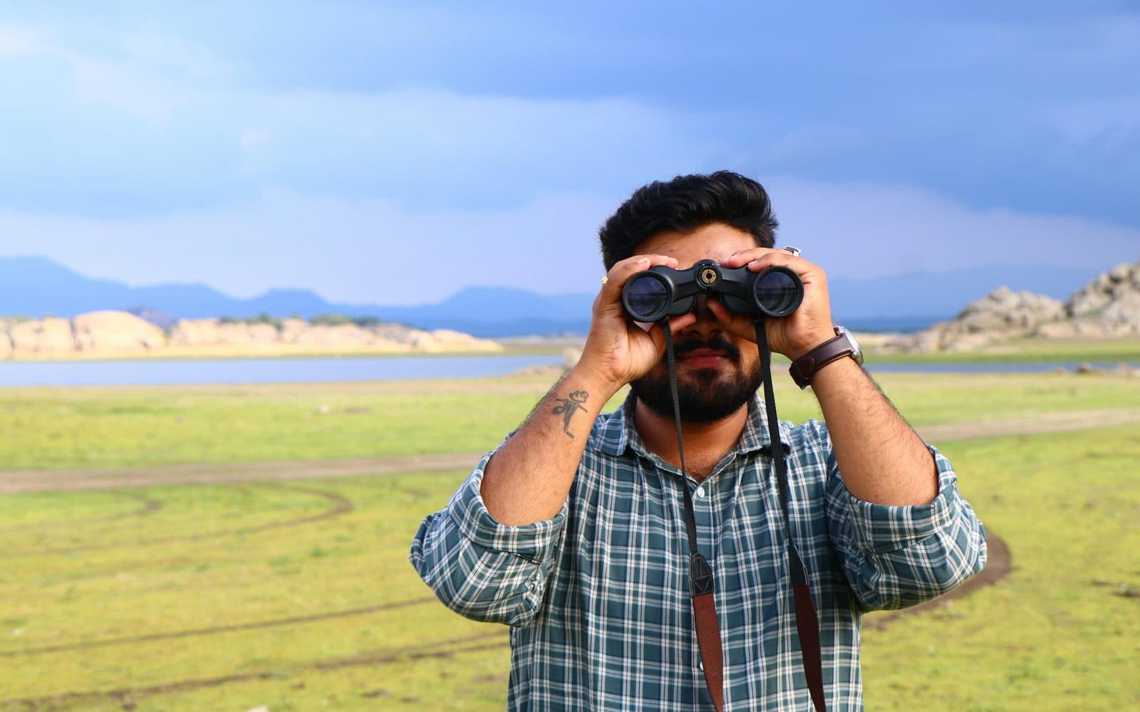 A man looking through binoculars across open countryside